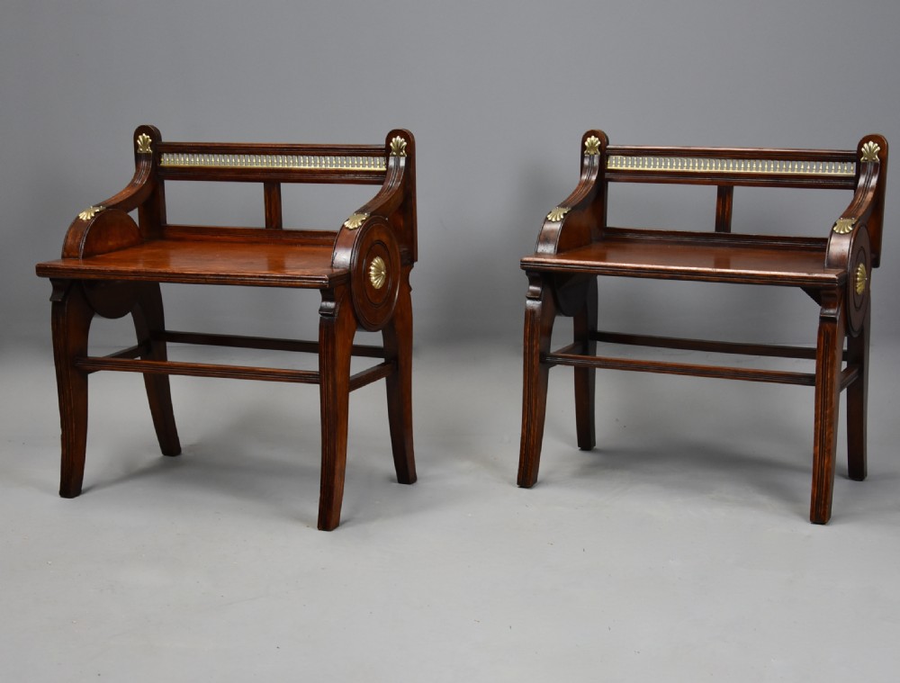 A pair of late nineteenth-century dark oak hall benches featuring carved side roundels, brass mounts, and a spindle gallery back. View II