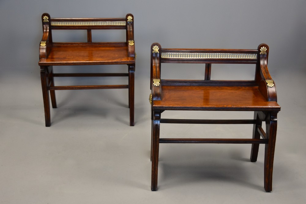 A pair of late nineteenth-century dark oak hall benches featuring carved side roundels, brass mounts, and a spindle gallery back. View V