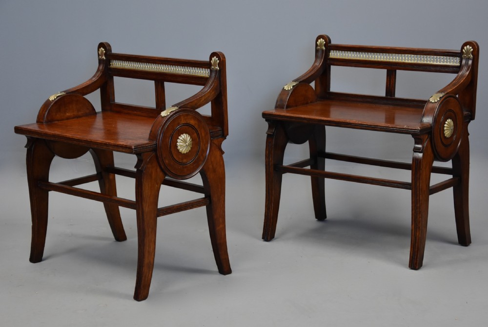 A pair of late nineteenth-century dark oak hall benches featuring carved side roundels, brass mounts, and a spindle gallery back. View VI