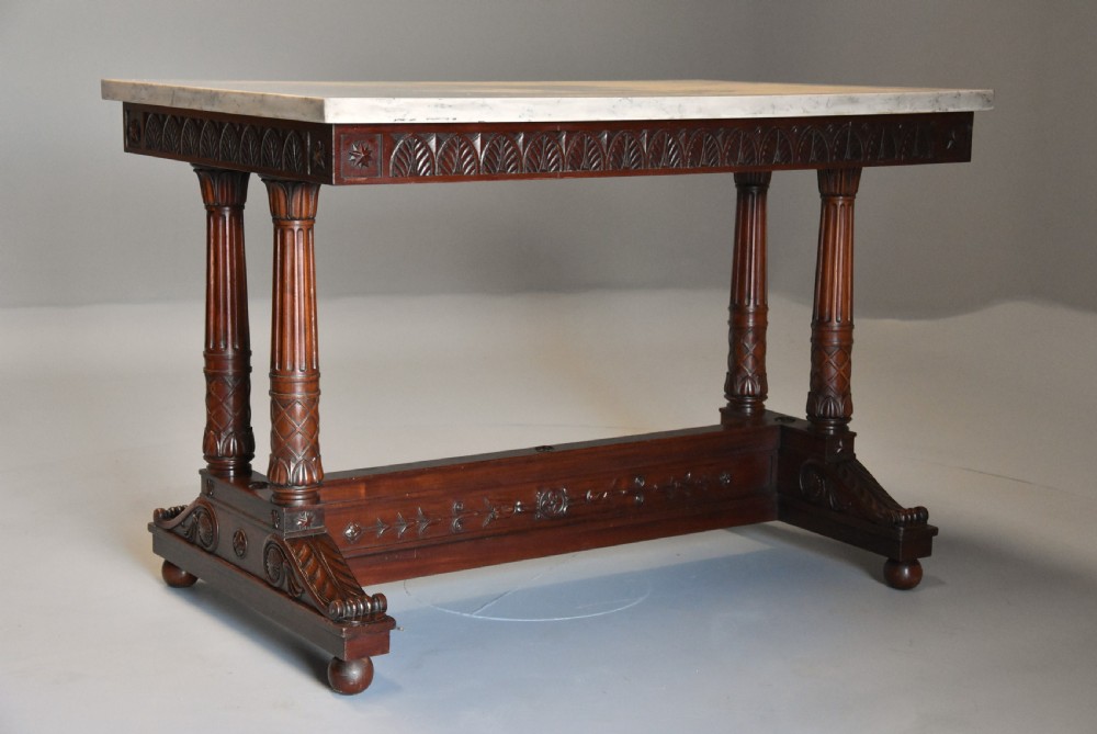 An early 19th-century French Empire mahogany centre table featuring a light marble top, carved frieze, fluted columns, and a trestle base. View II