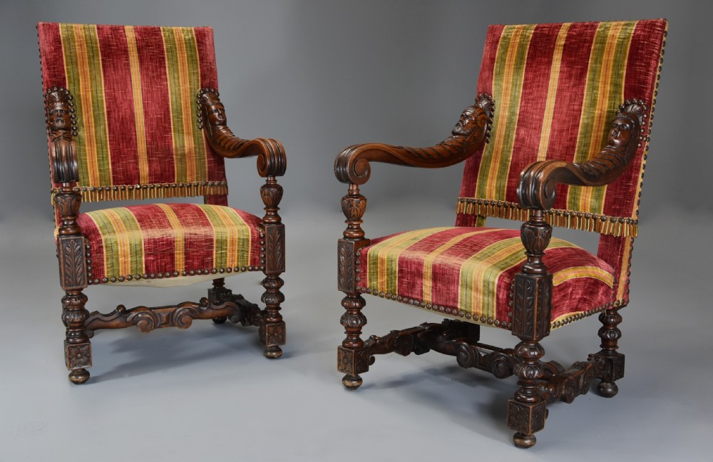 Pair of nineteenth-century French Baroque style walnut open armchairs upholstered in striped red and green velvet with carved human mask armrests.