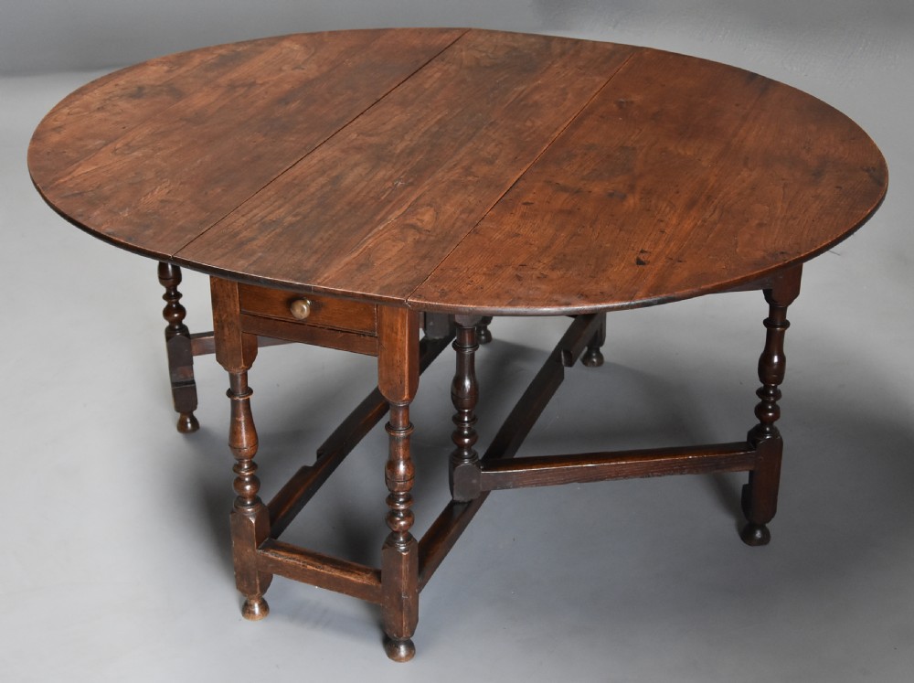 A late 17th-century oak gateleg dining table with an oval drop-leaf top, turned legs, and a small single end drawer.
