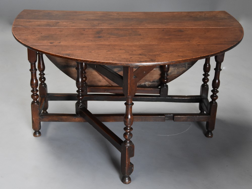 A late 17th-century oak gateleg dining table with an oval drop-leaf top, turned legs, and a small single end drawer. View V