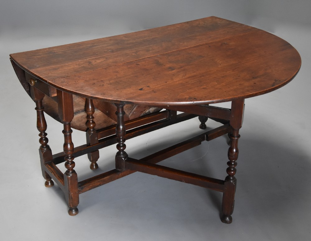 A late 17th-century oak gateleg dining table with an oval drop-leaf top, turned legs, and a small single end drawer. View VI