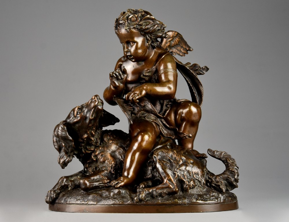 A late 19th-century dark patinated bronze sculpture depicting a winged putto interacting with a recumbent spaniel dog on an oval base.