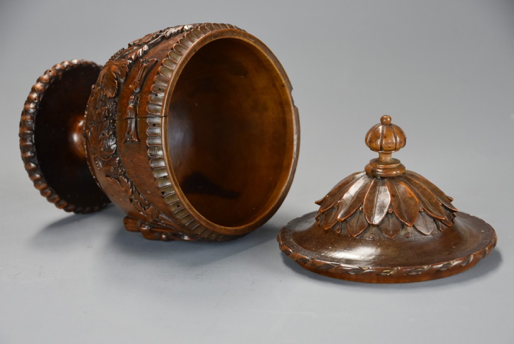 A late eighteenth-century carved walnut lidded urn featuring floral garlands, tassel motifs, a leaf-carved dome lid with finial, resting on a turned circular base. View XIII