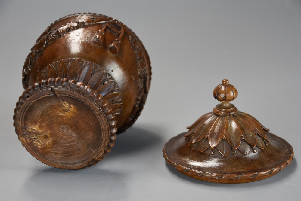 A late eighteenth-century carved walnut lidded urn featuring floral garlands, tassel motifs, a leaf-carved dome lid with finial, resting on a turned circular base. View XIV
