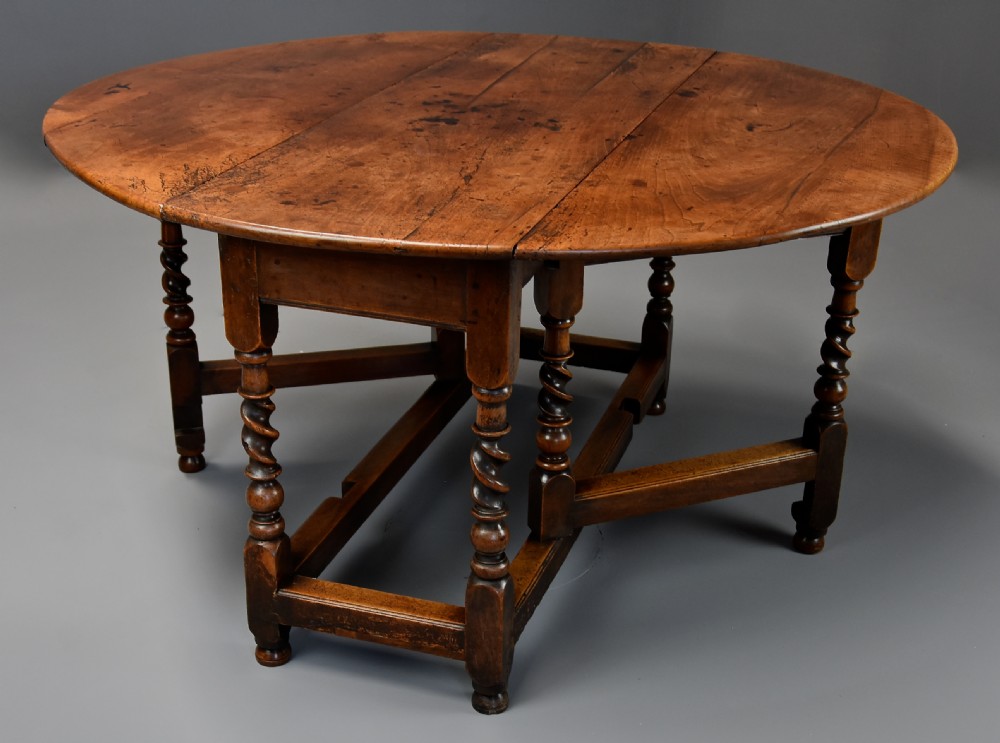 A 17th-century walnut gateleg table with extended oval drop leaves and double barley twist turned legs supported by stretchers.