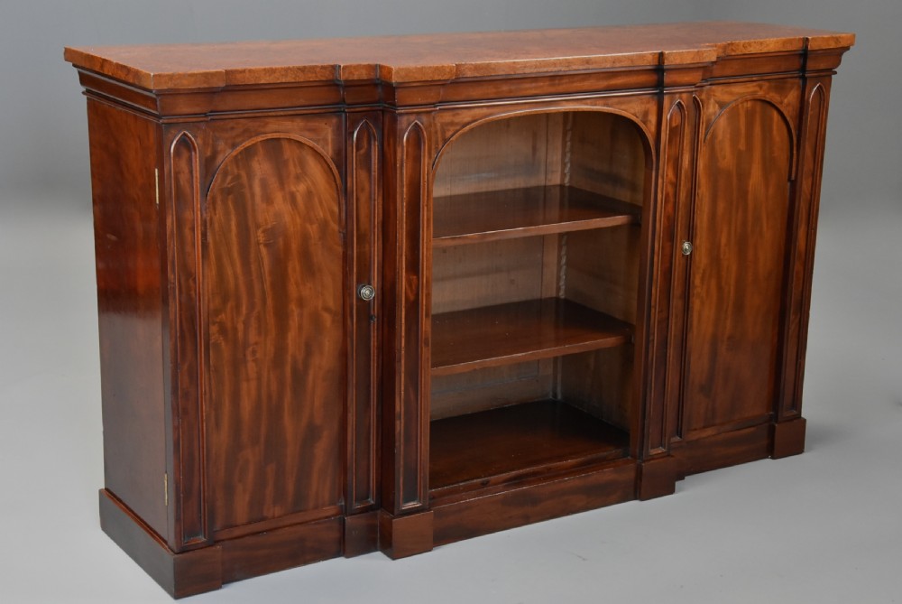 A mid-19th century mahogany breakfront low bookcase featuring pointed Gothic arch details, flanked by two panelled cupboard doors and an open central shelving area. View IV