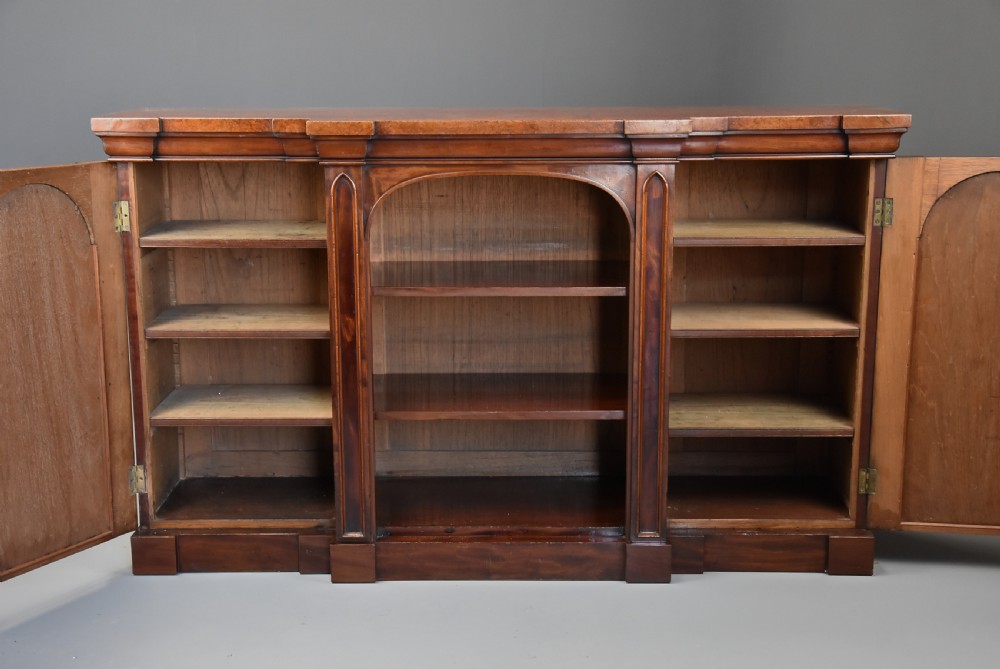 A mid-19th century mahogany breakfront low bookcase featuring pointed Gothic arch details, flanked by two panelled cupboard doors and an open central shelving area. View VIII