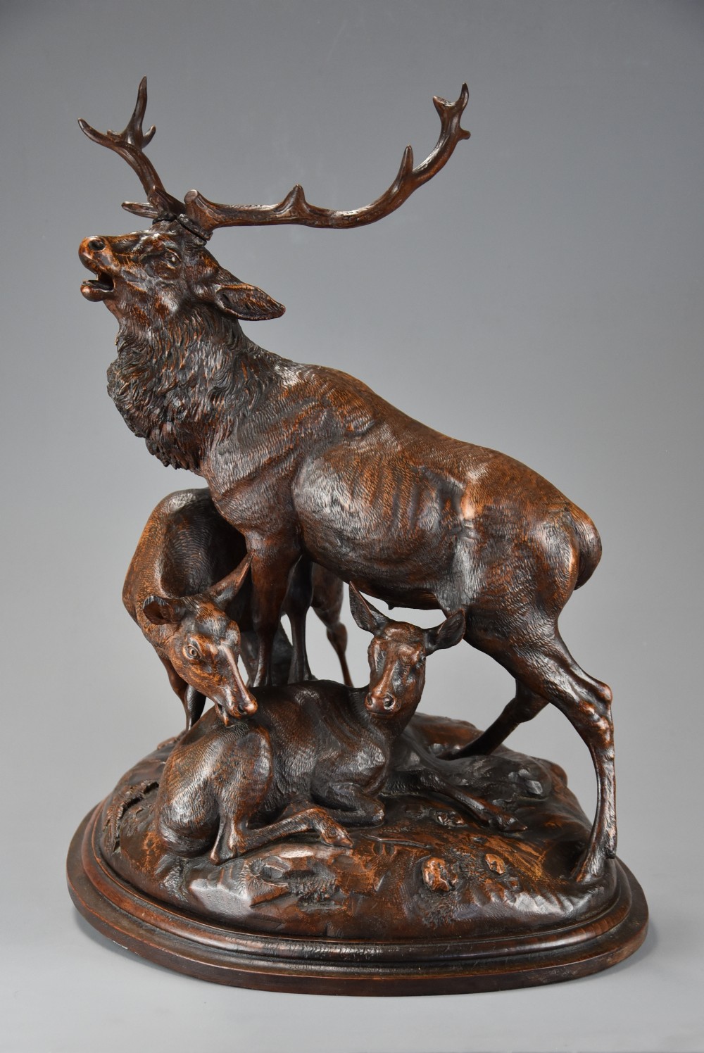 A late 19th-century dark carved linden wood sculpture depicting a roaring stag standing above a doe and lying fawn on a naturalistic base.