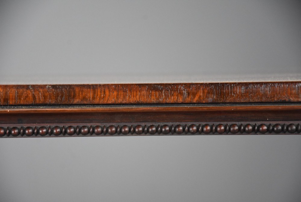 A William IV rosewood centre writing table featuring a rectangular top, beaded border, carved end supports, a central turned stretcher, and lobed feet. View X