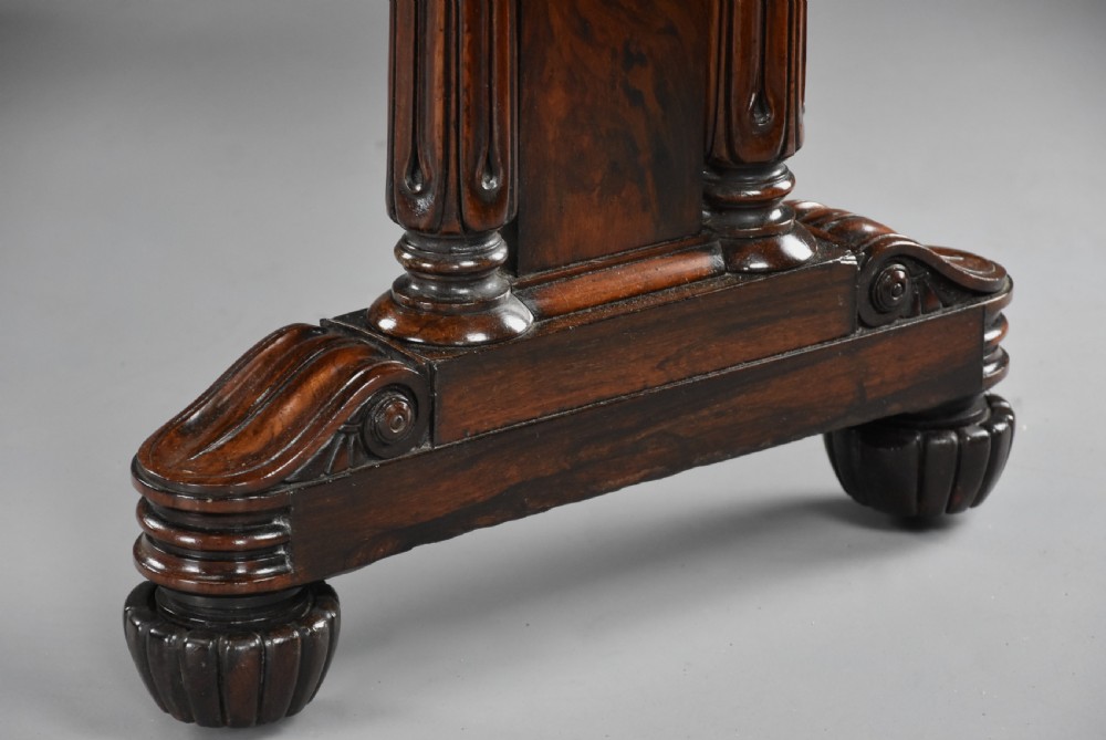 A William IV rosewood centre writing table featuring a rectangular top, beaded border, carved end supports, a central turned stretcher, and lobed feet. View XIV