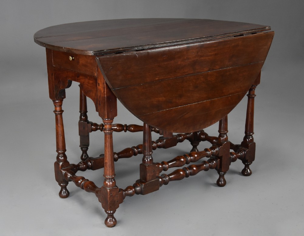 An 18th-century dark walnut gateleg table with folding drop leaves, turned supports, and lower stretchers.
