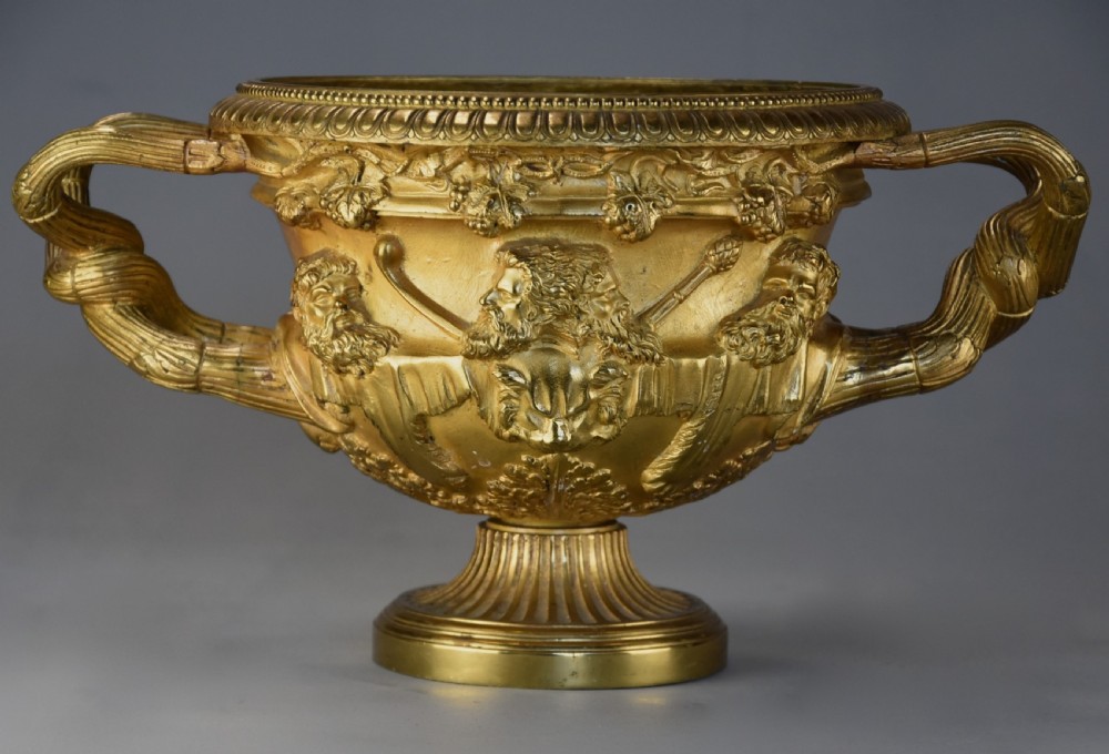 A 19th-century gilt bronze reduction of the Warwick Vase featuring high-relief Bacchic masks, intertwined vine handles, and a pedestal base.