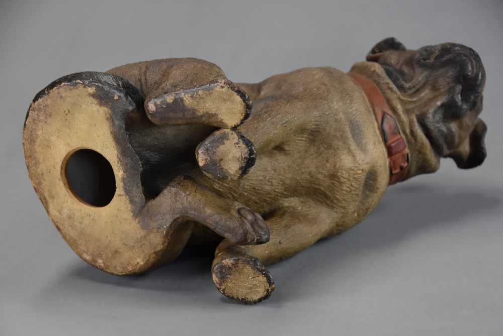 A late 19th-century painted terracotta figure of a seated pug dog with brown fur, a red collar, and glass eyes, set against a plain grey background. View XIII