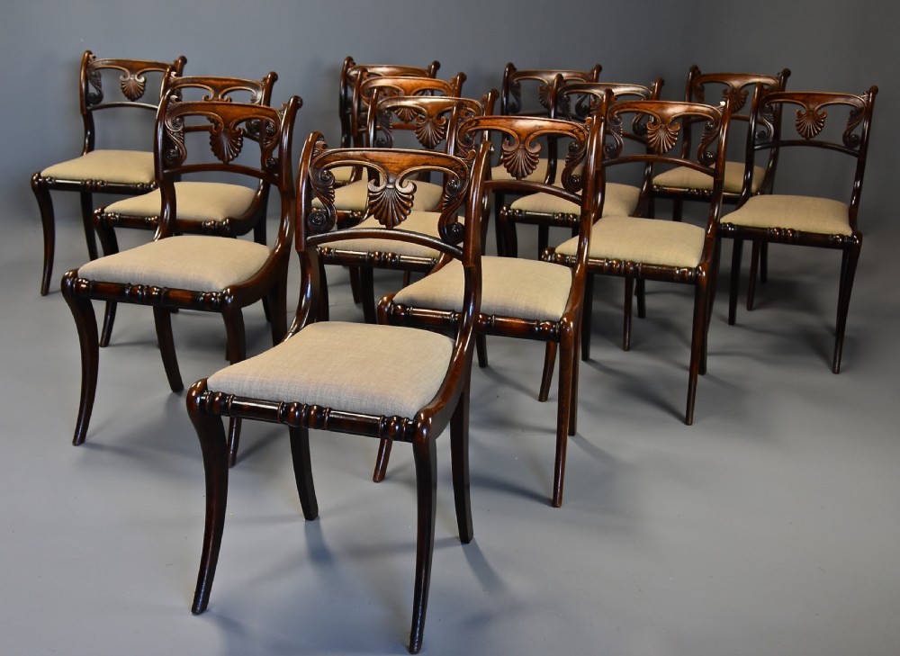 A set of thirteen early nineteenth-century Regency dining chairs featuring carved anthemion backrests, curved legs, and light neutral upholstered seat cushions. View II