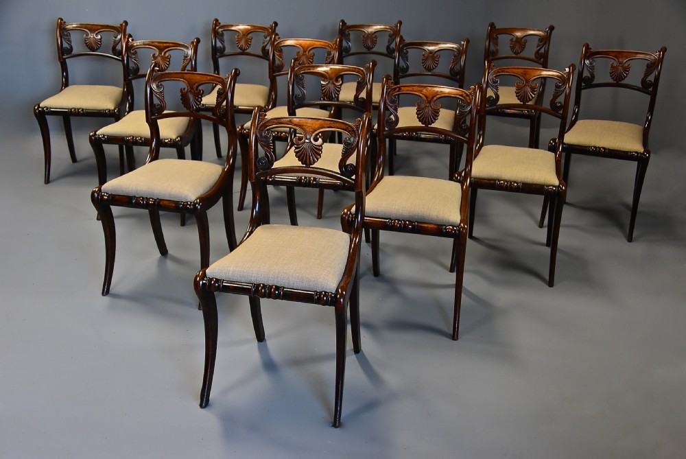 A set of thirteen early nineteenth-century Regency dining chairs featuring carved anthemion backrests, curved legs, and light neutral upholstered seat cushions. View III