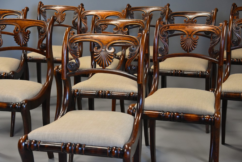 A set of thirteen early nineteenth-century Regency dining chairs featuring carved anthemion backrests, curved legs, and light neutral upholstered seat cushions. View IV