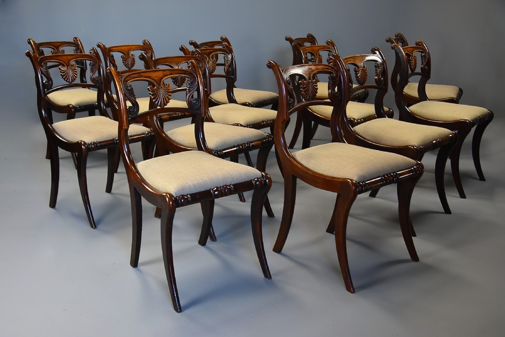 A set of thirteen early nineteenth-century Regency dining chairs featuring carved anthemion backrests, curved legs, and light neutral upholstered seat cushions. View V