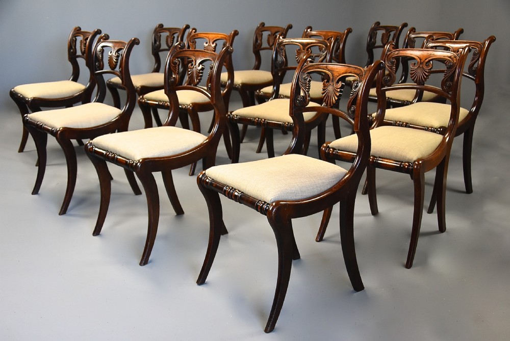 A set of thirteen early nineteenth-century Regency dining chairs featuring carved anthemion backrests, curved legs, and light neutral upholstered seat cushions. View VII