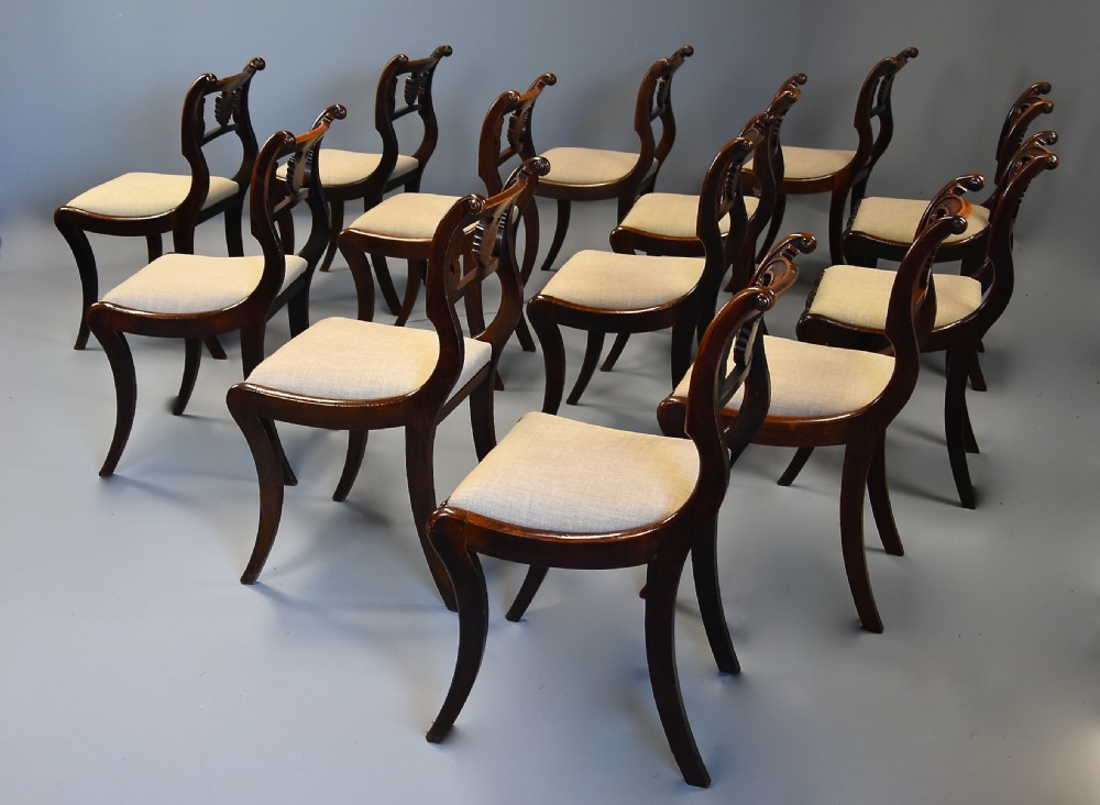 A set of thirteen early nineteenth-century Regency dining chairs featuring carved anthemion backrests, curved legs, and light neutral upholstered seat cushions. View VIII