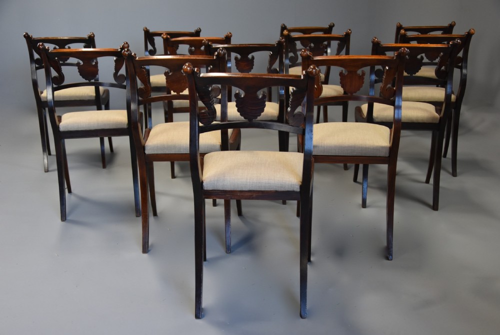 A set of thirteen early nineteenth-century Regency dining chairs featuring carved anthemion backrests, curved legs, and light neutral upholstered seat cushions. View IX