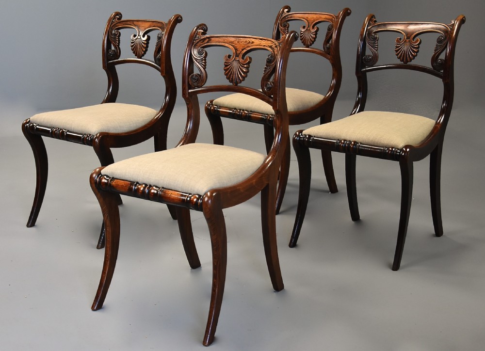 A set of thirteen early nineteenth-century Regency dining chairs featuring carved anthemion backrests, curved legs, and light neutral upholstered seat cushions. View XII