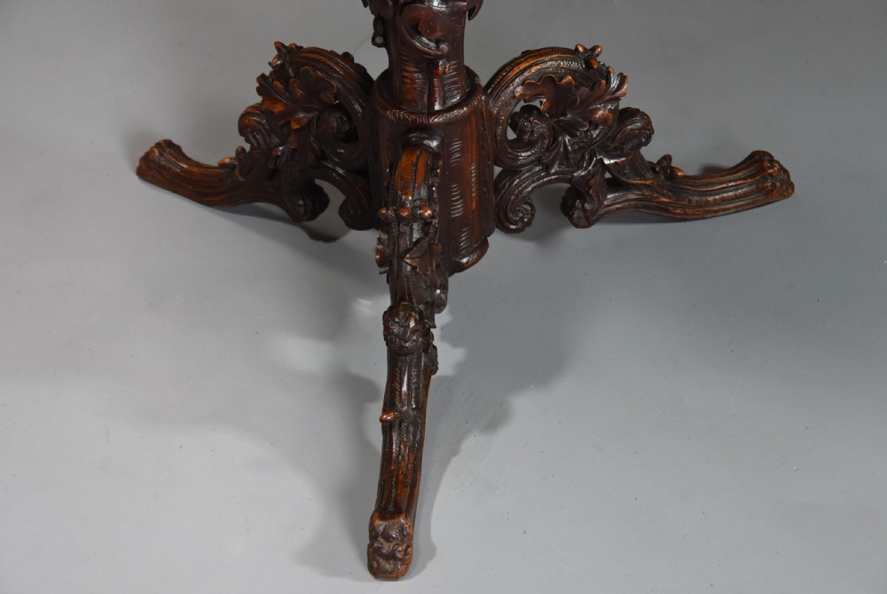 A circular late 19th-century dark brown linden wood centre table featuring intricate foliate carvings on the top, a decorated pedestal, and a tripod base. View VIII