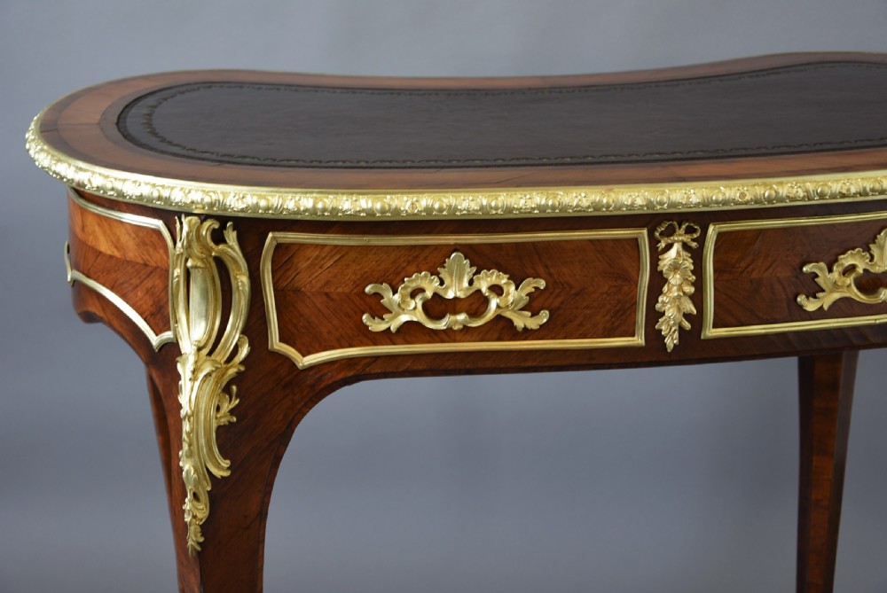 A 19th-century kidney-shaped kingwood writing desk featuring gilt-bronze ormolu mounts, a leather top, and curved cabriole legs. View XIII