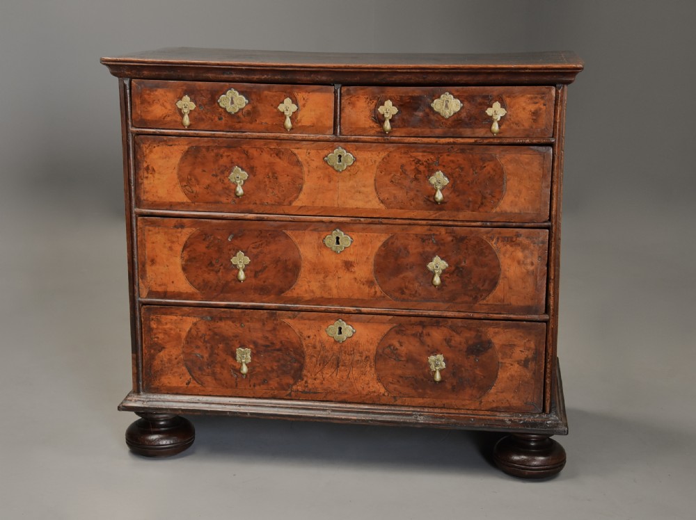 A late 17th-century William and Mary chest of drawers with oval yew wood veneers, brass teardrop handles, and dark turned bun feet. View V