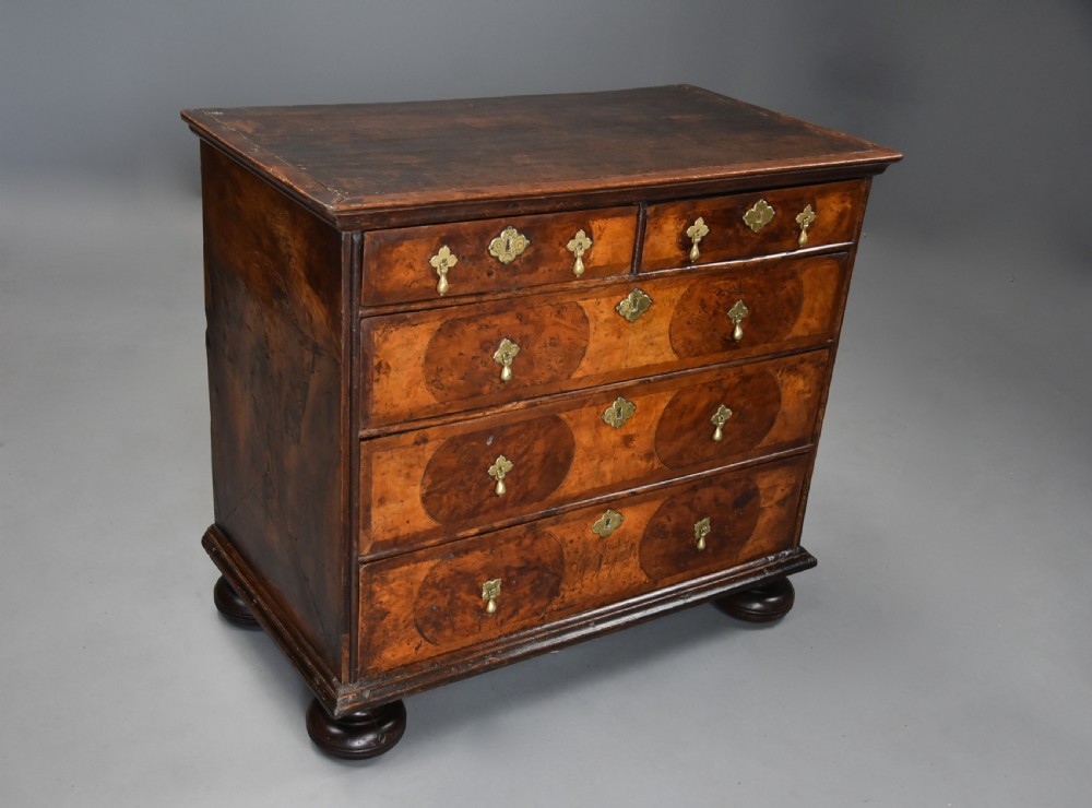 A late 17th-century William and Mary chest of drawers with oval yew wood veneers, brass teardrop handles, and dark turned bun feet. View VI