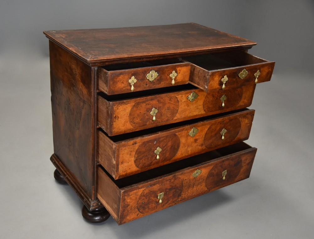 A late 17th-century William and Mary chest of drawers with oval yew wood veneers, brass teardrop handles, and dark turned bun feet. View VII