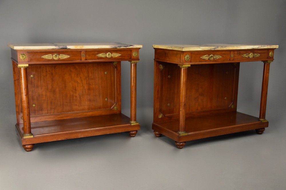 A pair of 19th-century French Empire style mahogany console tables featuring light marble tops, gilt bronze mounts, and cylindrical front columns. View IV