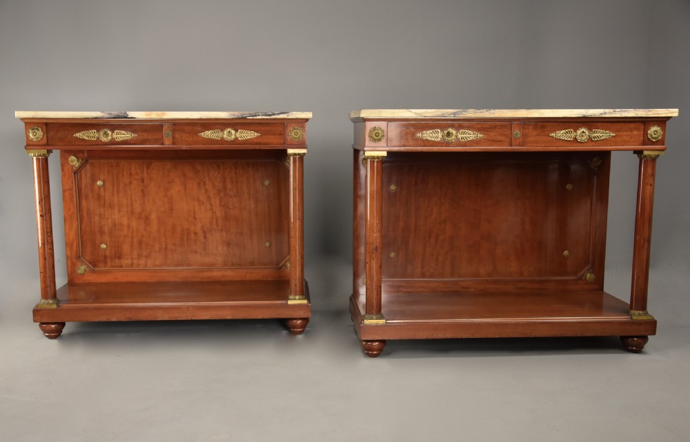 A pair of 19th-century French Empire style mahogany console tables featuring light marble tops, gilt bronze mounts, and cylindrical front columns. View V