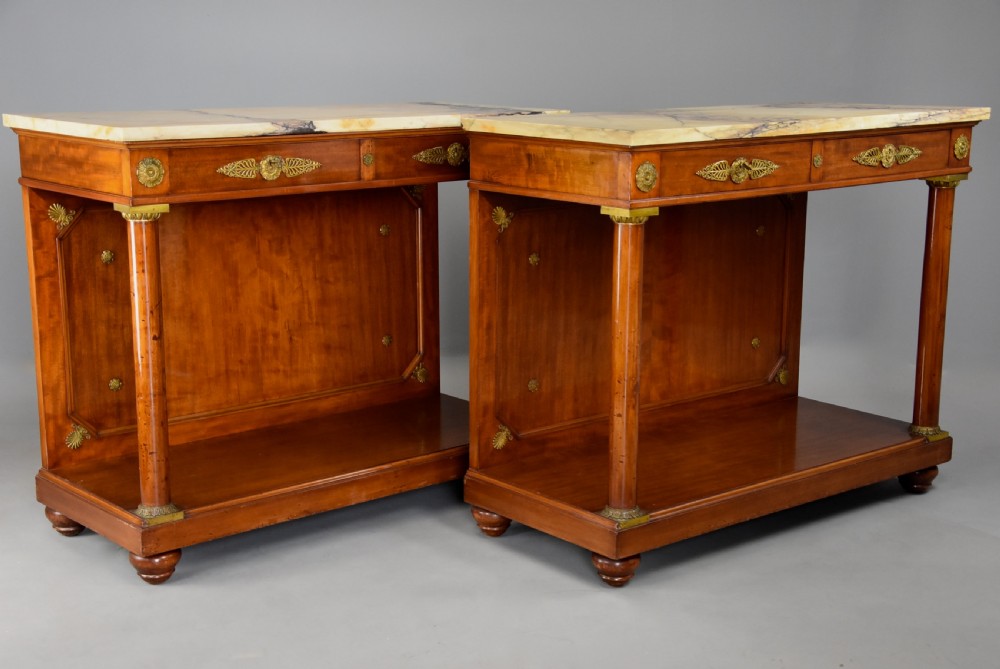 A pair of 19th-century French Empire style mahogany console tables featuring light marble tops, gilt bronze mounts, and cylindrical front columns. View VI