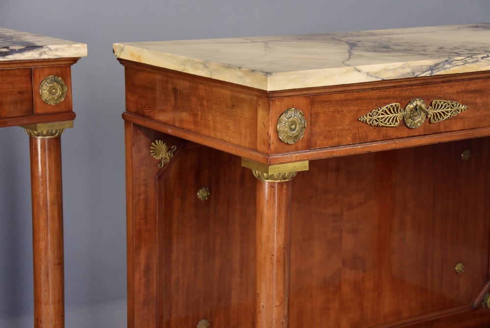A pair of 19th-century French Empire style mahogany console tables featuring light marble tops, gilt bronze mounts, and cylindrical front columns. View IX