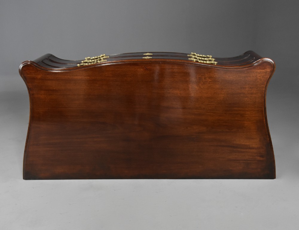 A late nineteenth-century dark flame mahogany serpentine chest of drawers featuring three graduated drawers with decorative brass handles and a carved lower apron. View XIII