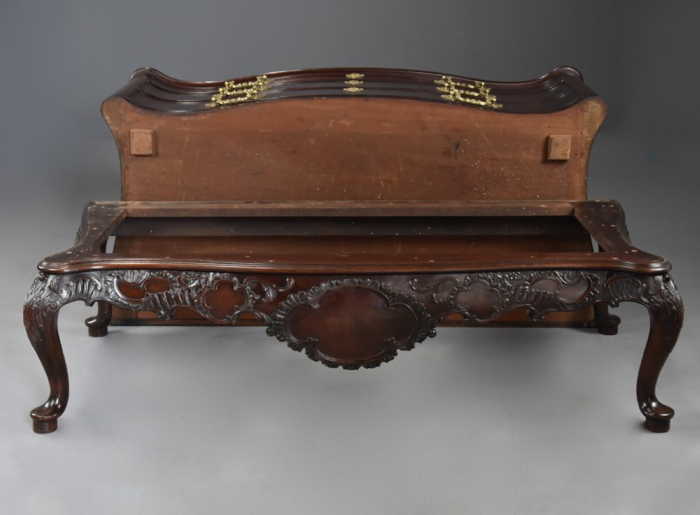 A late nineteenth-century dark flame mahogany serpentine chest of drawers featuring three graduated drawers with decorative brass handles and a carved lower apron. View XVI