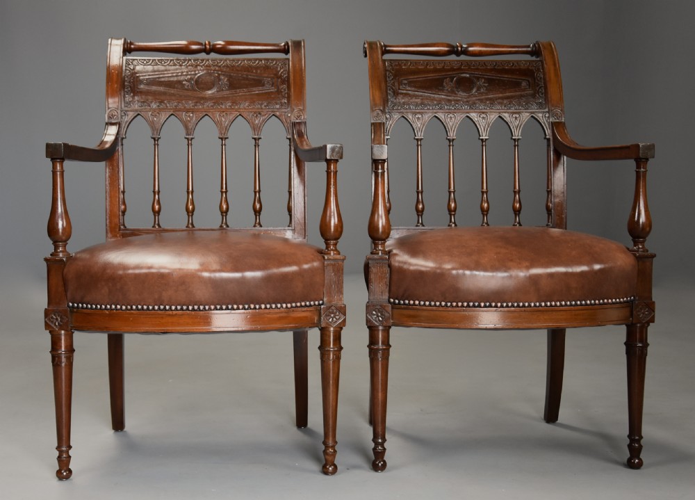 A pair of late 18th-century French Directoire style carved walnut open armchairs with studded brown leather seats. View V