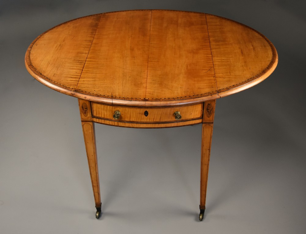 A late 18th-century Georgian Pembroke table made of fiddleback sycamore timber with two drop leaves, a single drawer with brass knobs, and tapered legs on brass castors. View V