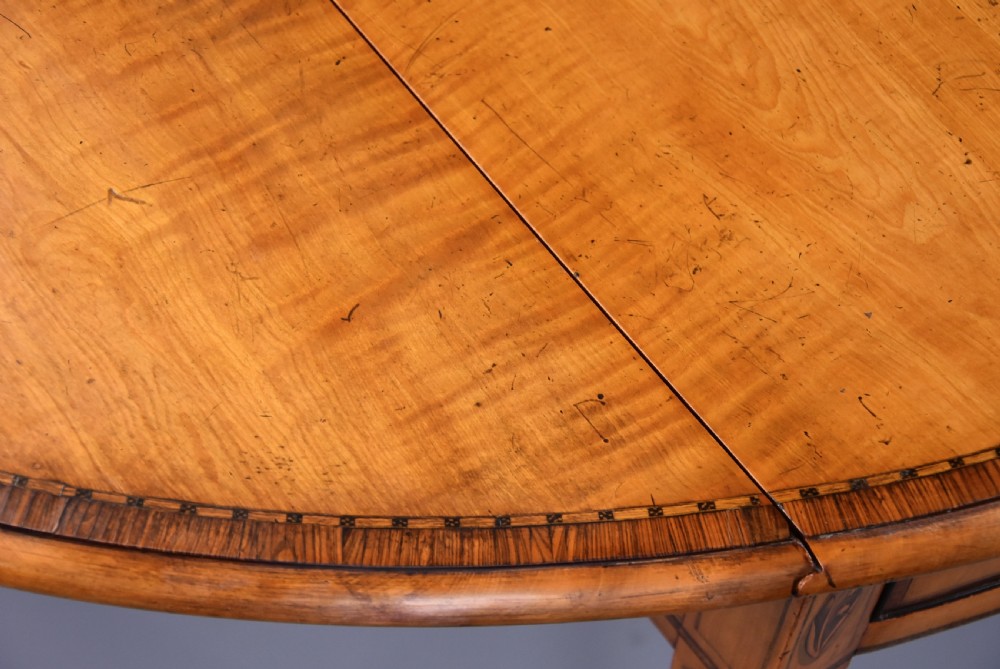 A late 18th-century Georgian Pembroke table made of fiddleback sycamore timber with two drop leaves, a single drawer with brass knobs, and tapered legs on brass castors. View XV