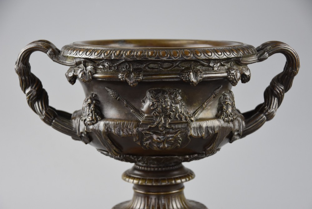 A late nineteenth-century patinated bronze reduction of the classical Warwick Vase featuring relief satyr masks and entwined handles, set upon a tiered yellow marble base. View VI