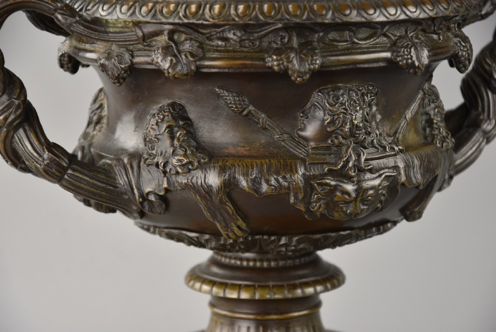 A late nineteenth-century patinated bronze reduction of the classical Warwick Vase featuring relief satyr masks and entwined handles, set upon a tiered yellow marble base. View VII