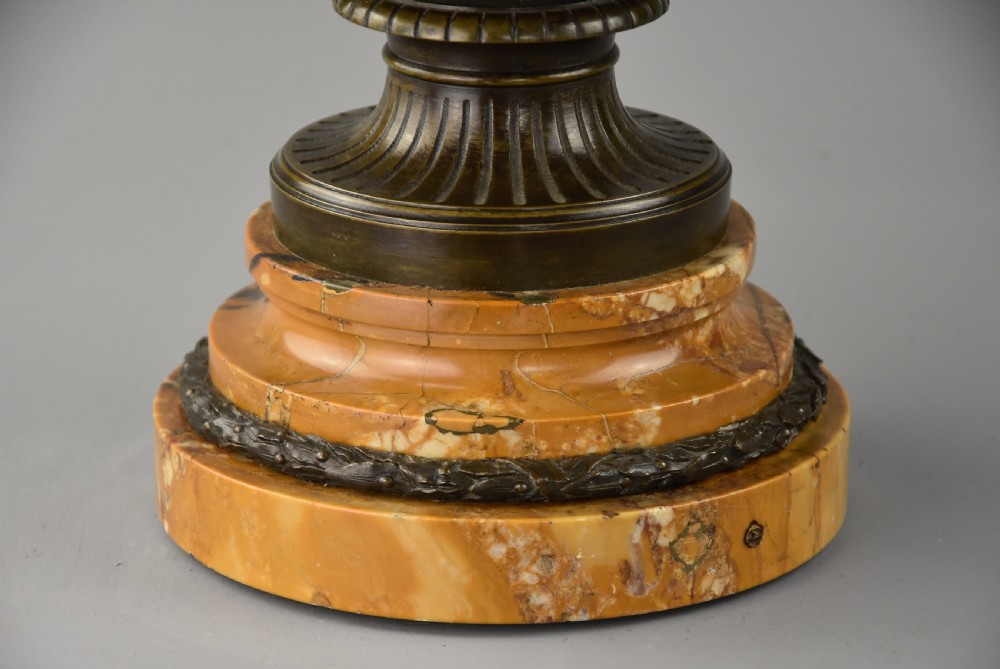 A late nineteenth-century patinated bronze reduction of the classical Warwick Vase featuring relief satyr masks and entwined handles, set upon a tiered yellow marble base. View IX