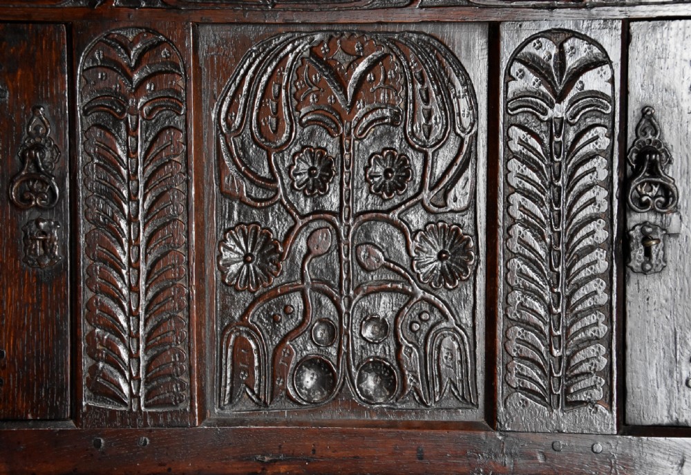 A 17th-century dark oak press cupboard featuring upper carved panel doors, overhanging canopy with pendant drops, and lower paneled double doors. View VII