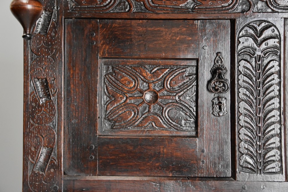 A 17th-century dark oak press cupboard featuring upper carved panel doors, overhanging canopy with pendant drops, and lower paneled double doors. View VIII