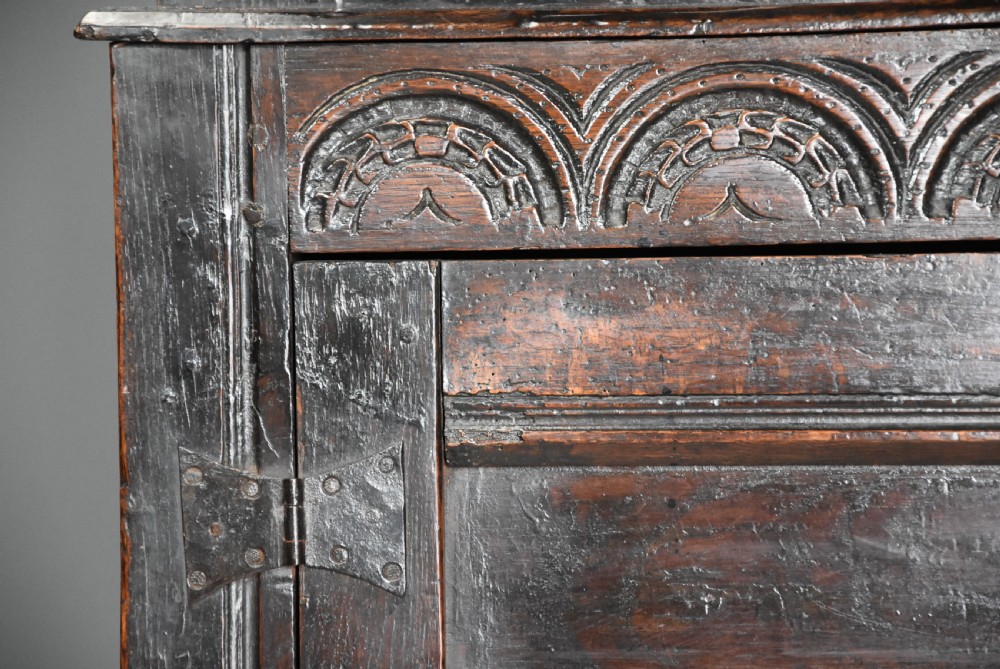 A 17th-century dark oak press cupboard featuring upper carved panel doors, overhanging canopy with pendant drops, and lower paneled double doors. View X