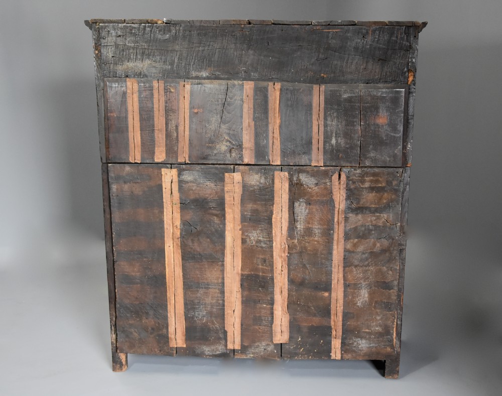 A 17th-century dark oak press cupboard featuring upper carved panel doors, overhanging canopy with pendant drops, and lower paneled double doors. View XIV