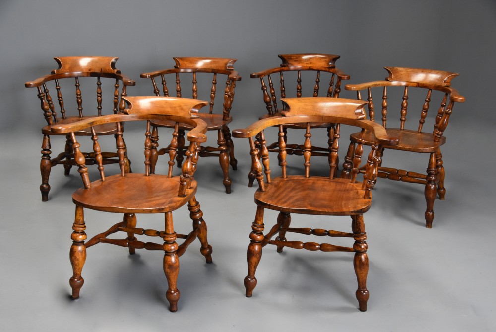 A set of six mid 19th century wooden smokers bow Windsor chairs with curved crest rails, turned spindles, shaped seats, and turned legs with stretchers.